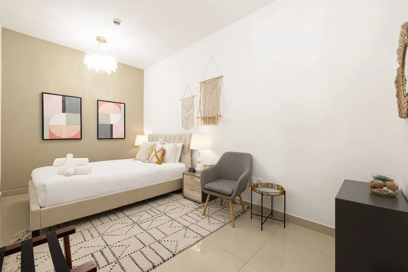 A bedroom with a bed, a gray armchair, and geometric wall art.