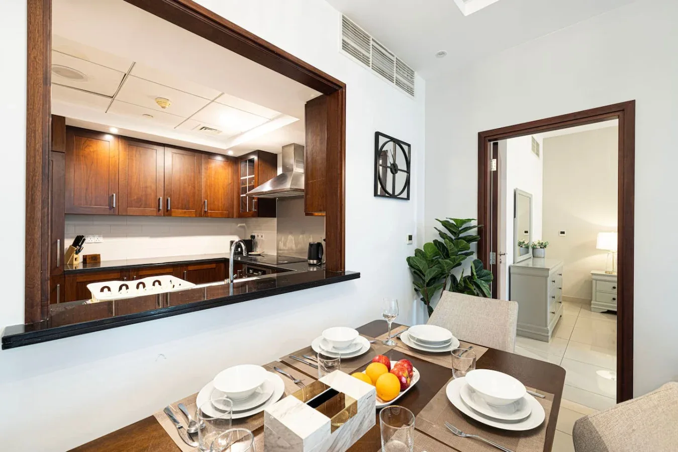 A dining area with a set table overlooks a kitchen through a wide pass-through.