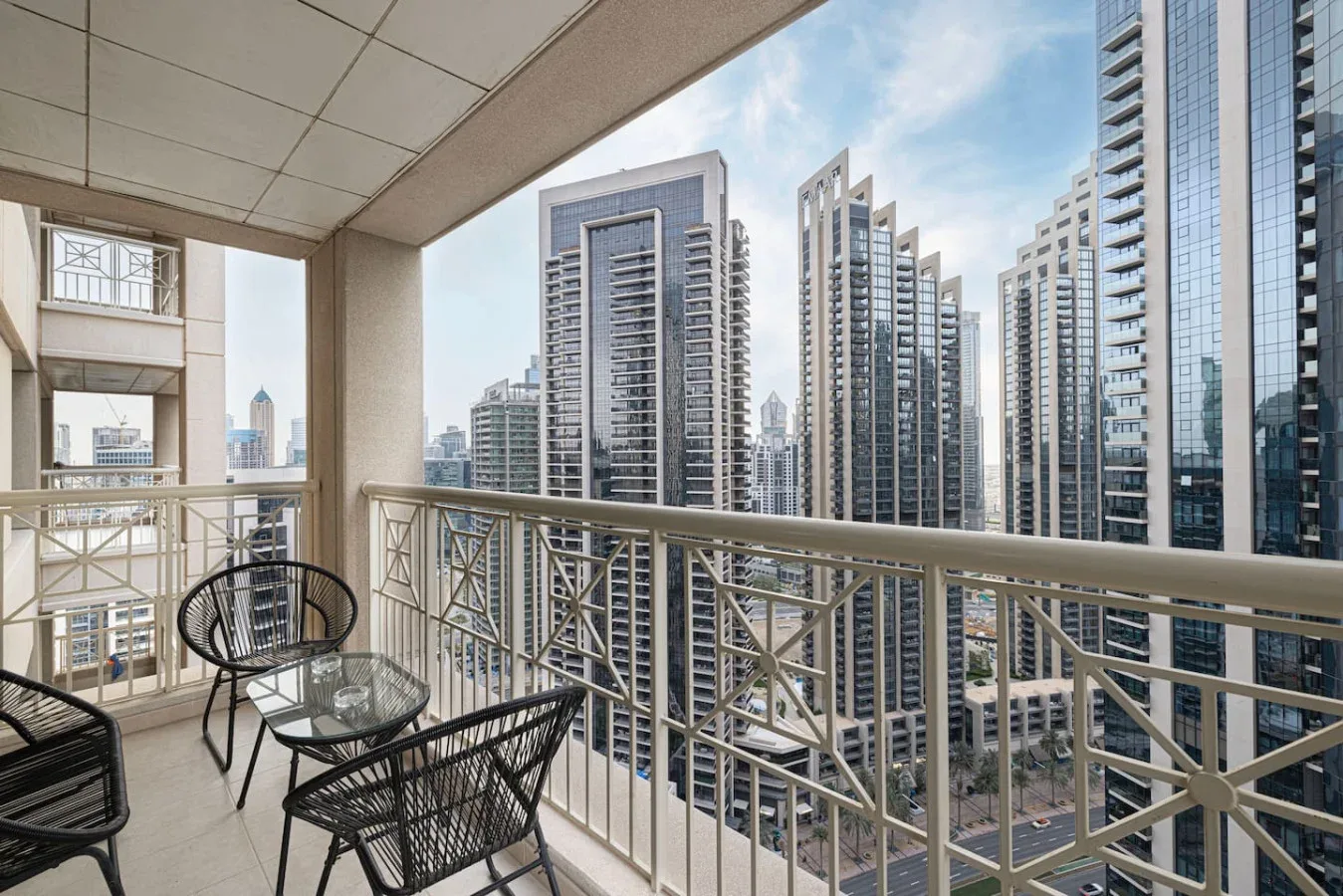 A balcony with metal railings and seating overlooks a cluster of high-rise buildings.
