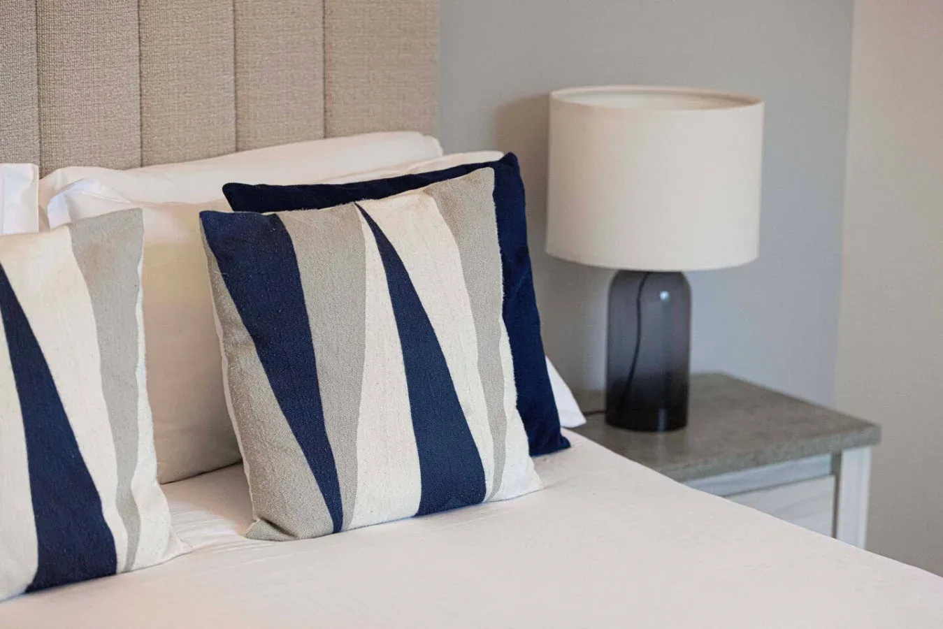 A bedroom with a neatly made bed, striped pillows, and a bedside lamp.