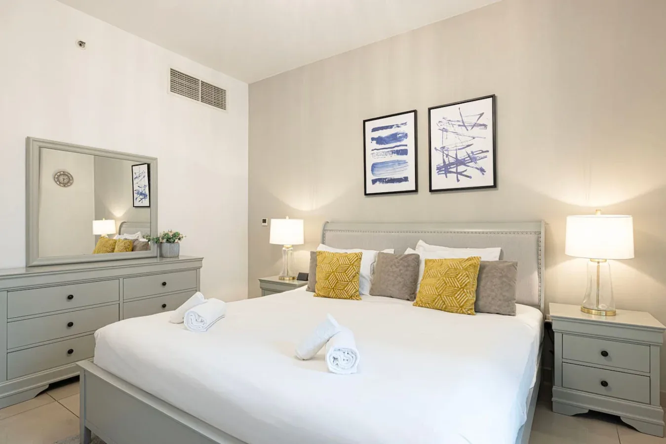 A bedroom with a large bed, bedside tables, and framed artwork above the headboard.