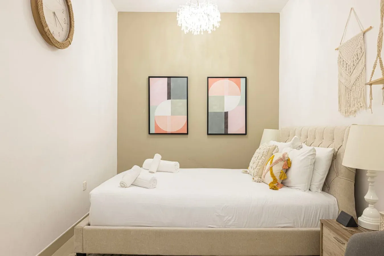 A bedroom with a neatly made bed and two framed abstract prints.