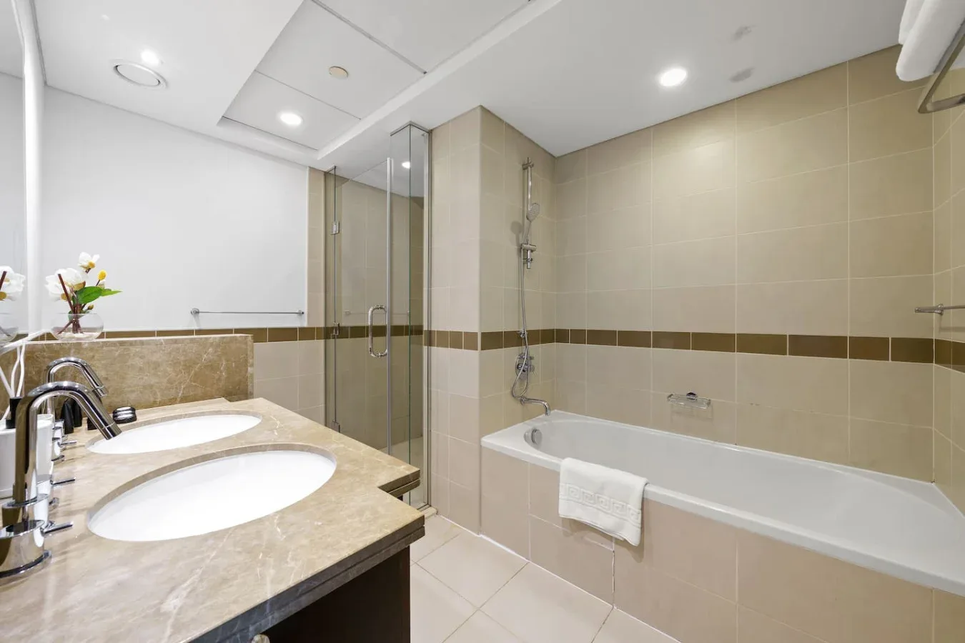 A tiled bathroom with a bathtub, glass shower, and double sink vanity.