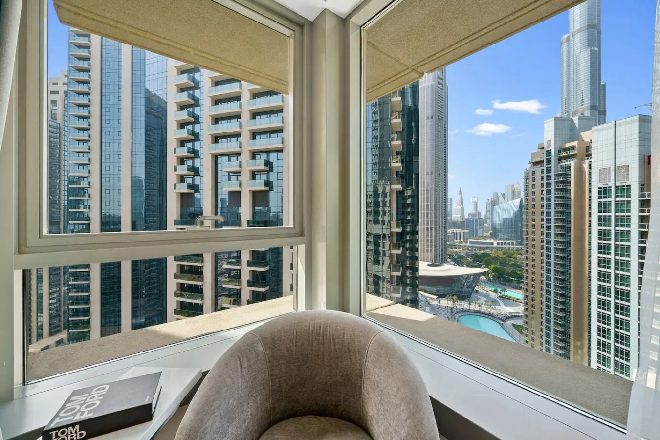A high-rise room corner overlooks surrounding towers and a blue swimming pool.