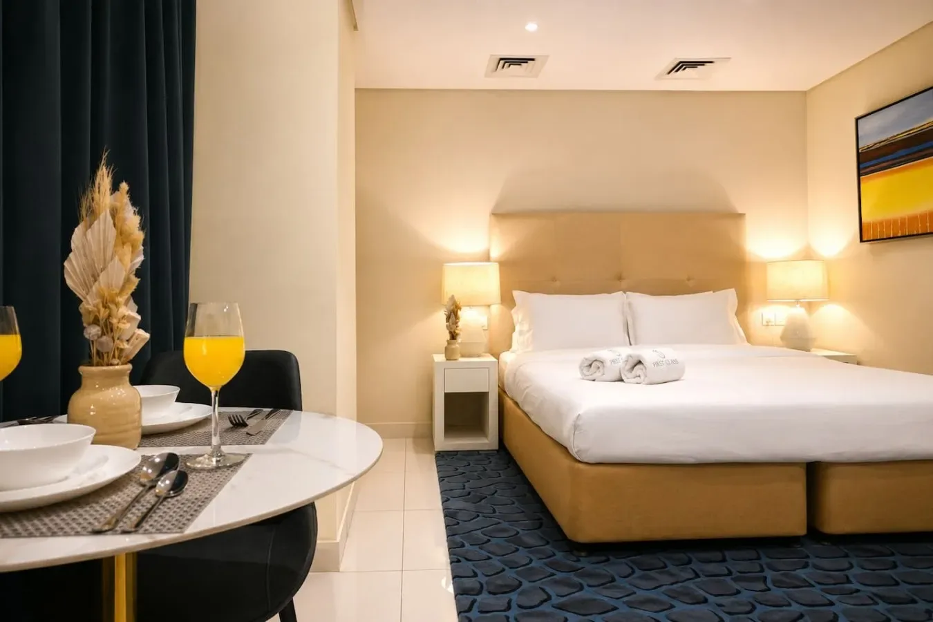 A bedroom with a neatly made bed and a small dining table beside it.
