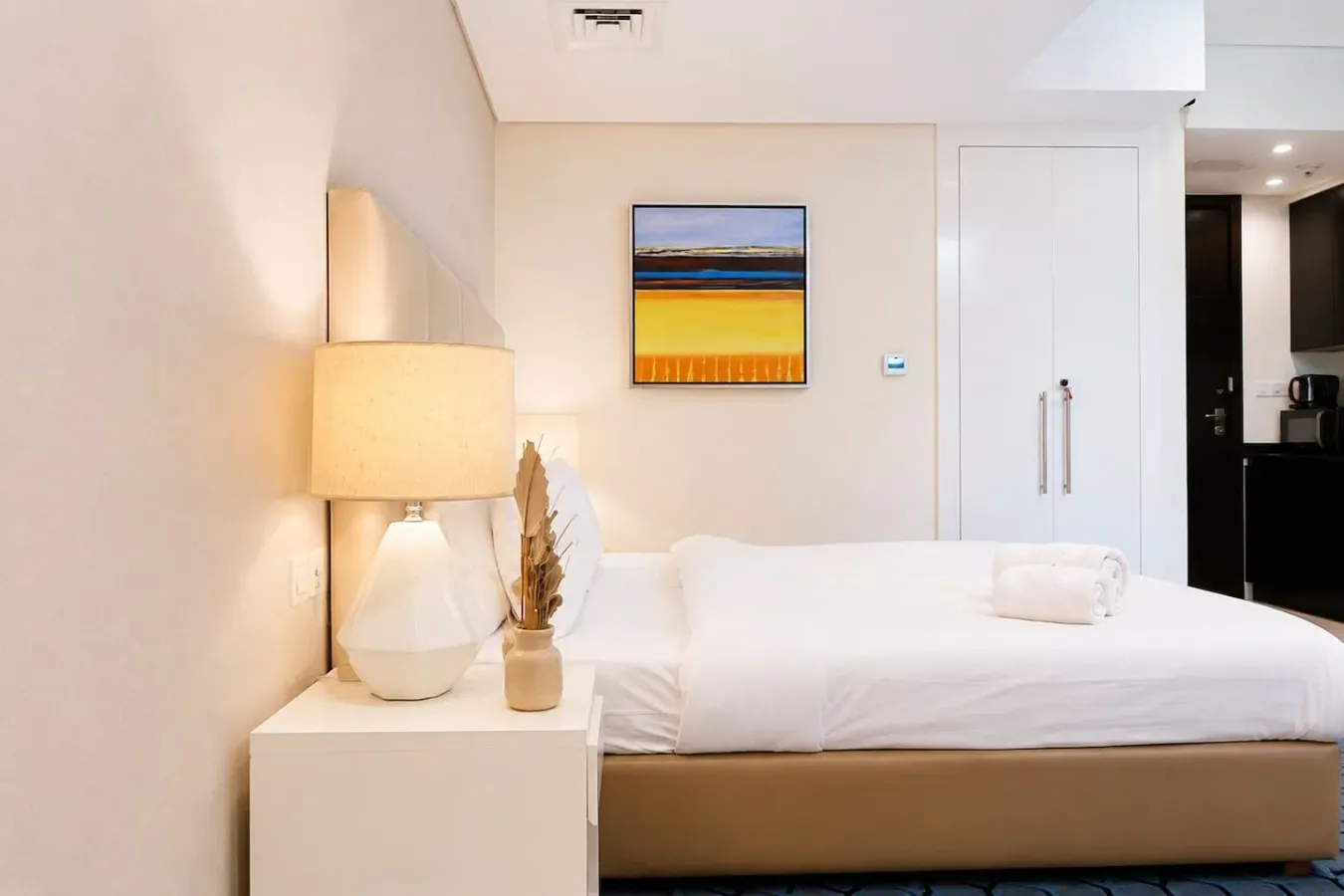 A bedroom with a neatly made bed and a framed colorful painting.