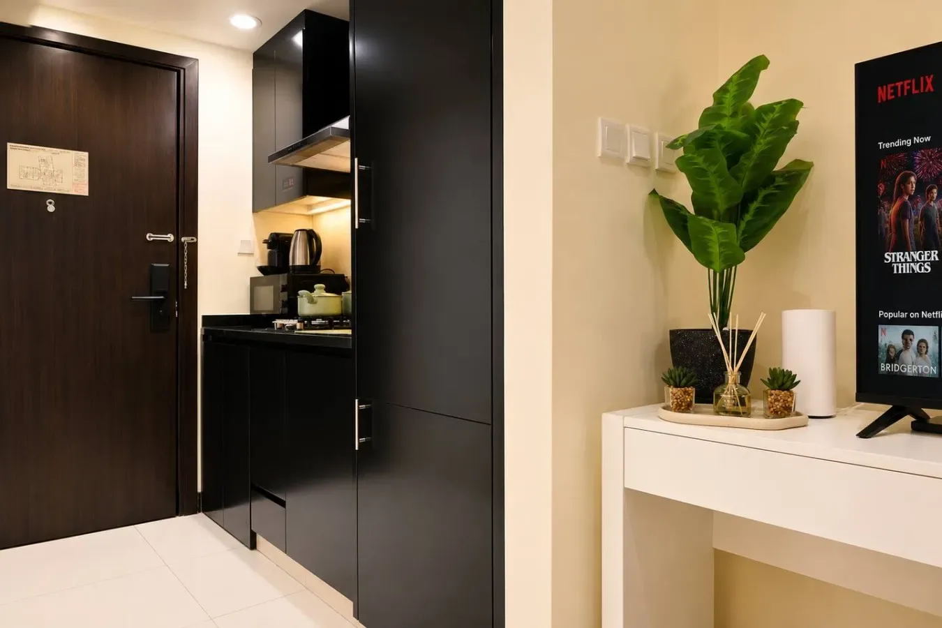 Una entrada compacta con gabinetes oscuros, una pequeña cocina y un televisor.