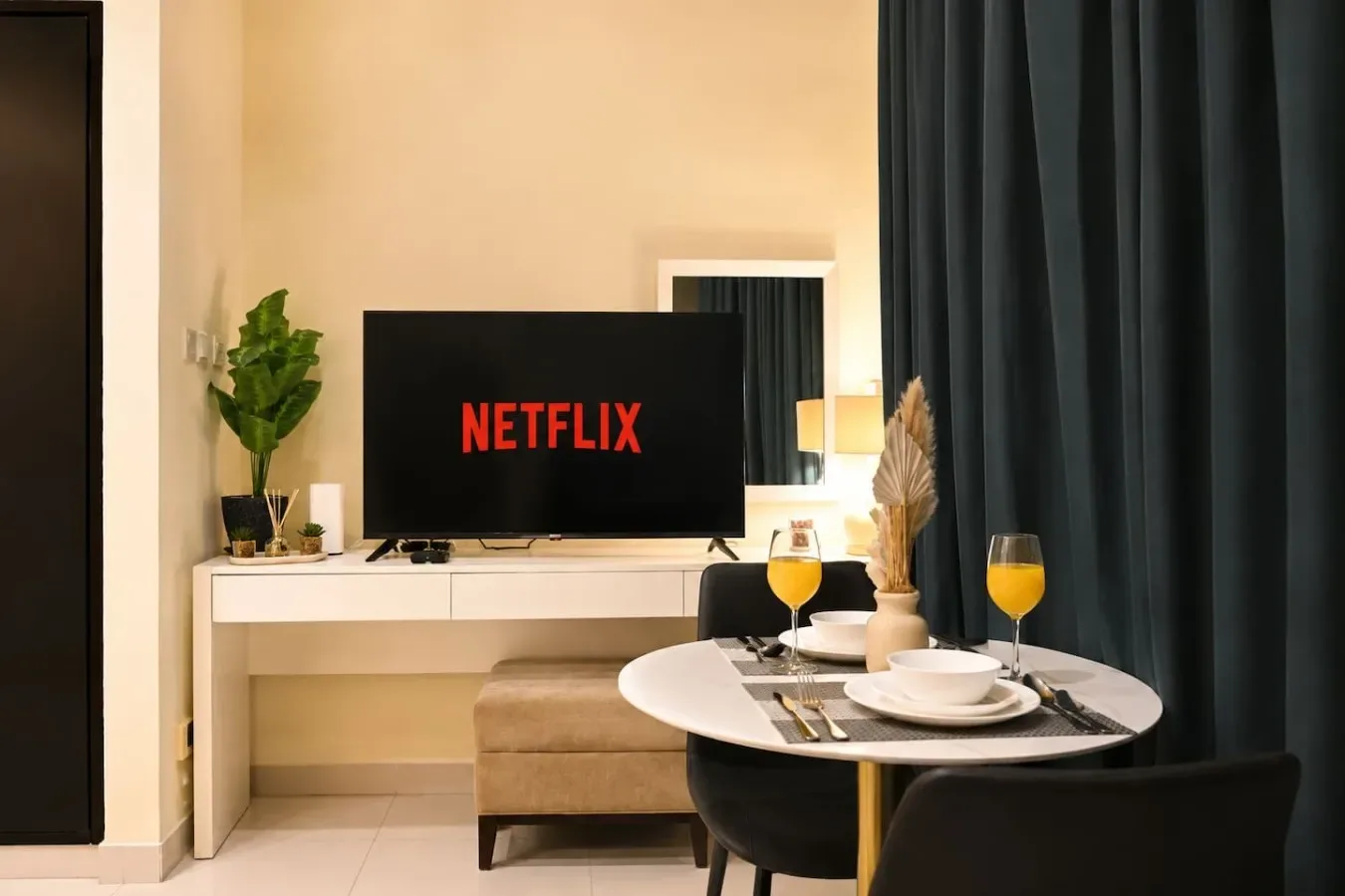 Un comedor con la mesa puesta junto a un televisor y cortinas oscuras.