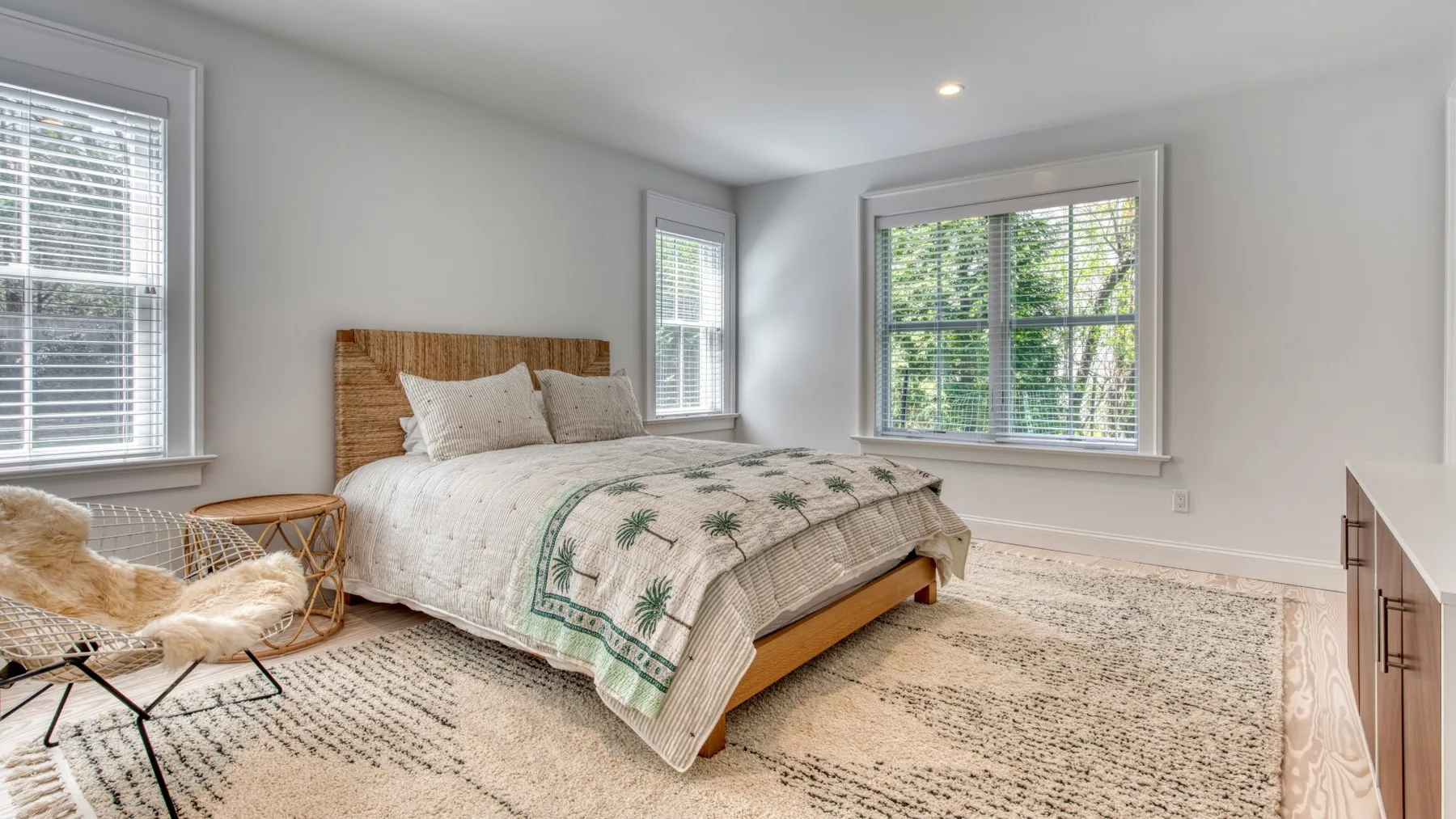 Un dormitorio luminoso con una cama junto a grandes ventanas con vistas a la vegetación.