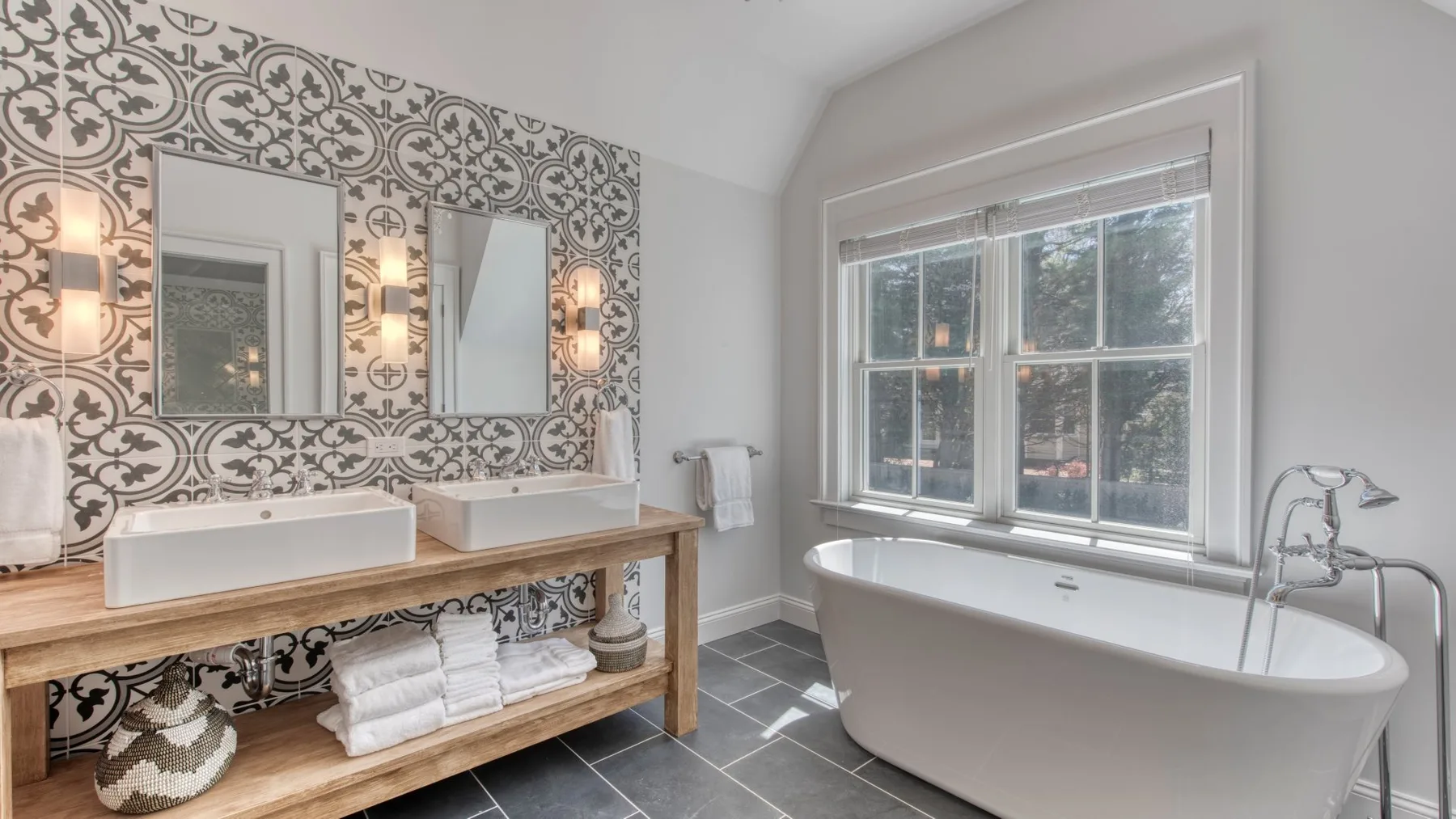 Un baño con bañera exenta, dos lavabos y azulejos estampados.