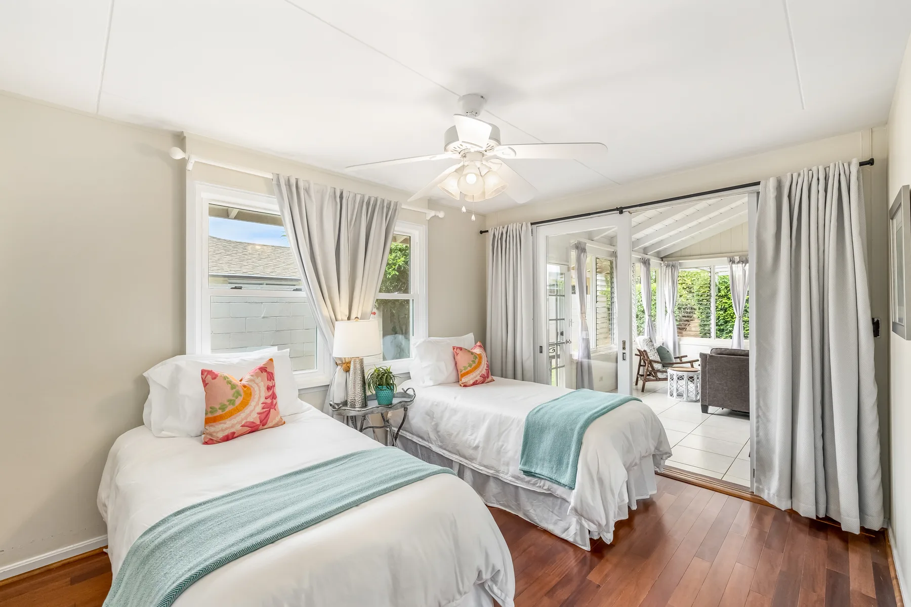A bright bedroom has two beds and sliding glass doors opening onto a patio.