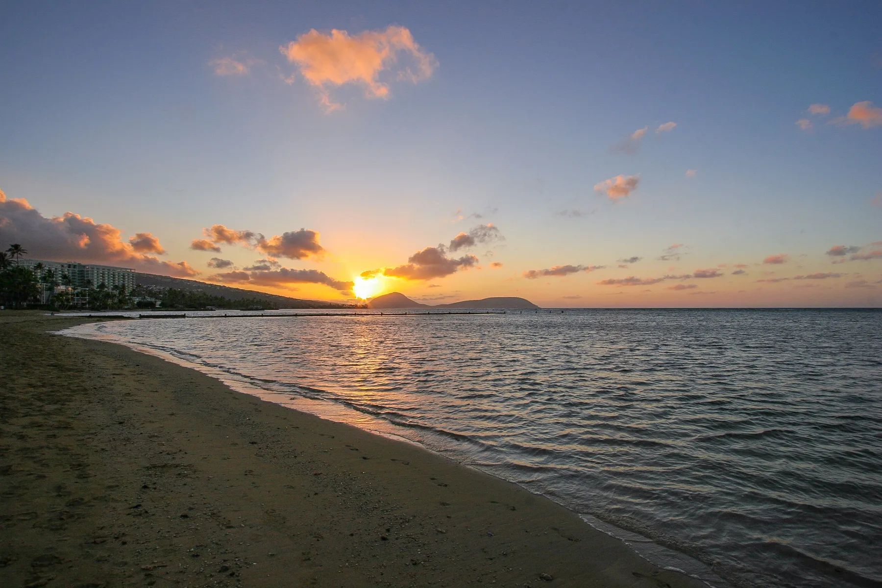 A sandy beach curves beside calm water beneath a sunset sky.
