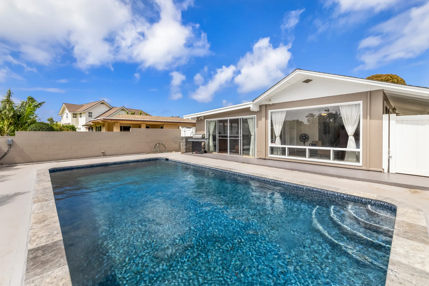 An outdoor swimming pool beside a single-story house under a partly cloudy sky.
