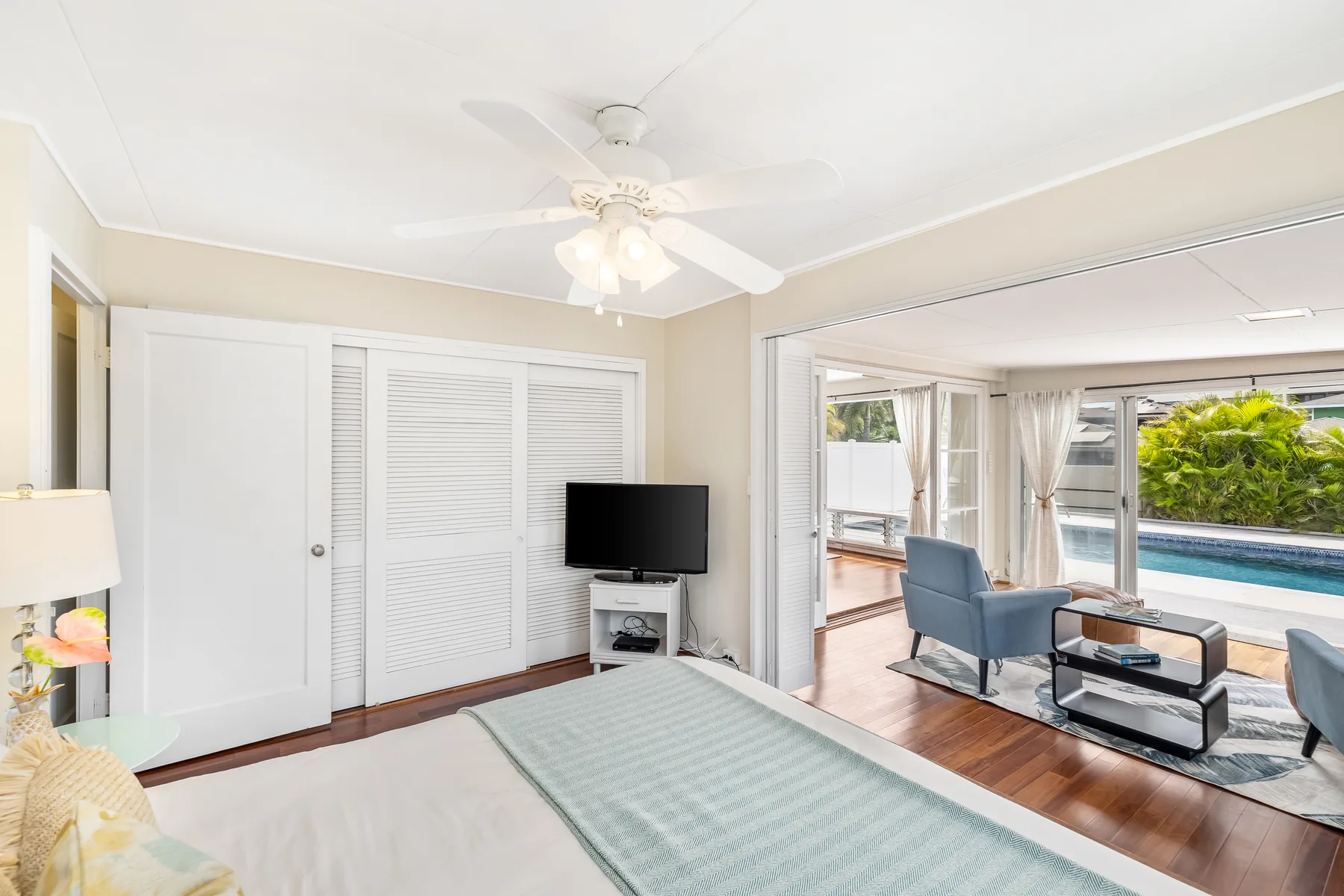 A bedroom with a bed and television opens onto a bright sitting area.