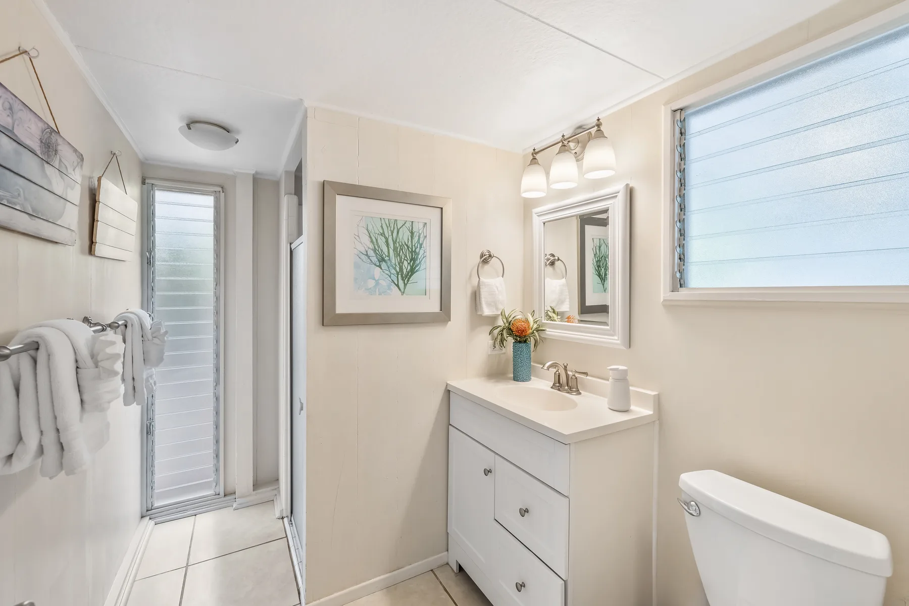 A bright bathroom with a sink vanity, mirror, and toilet.