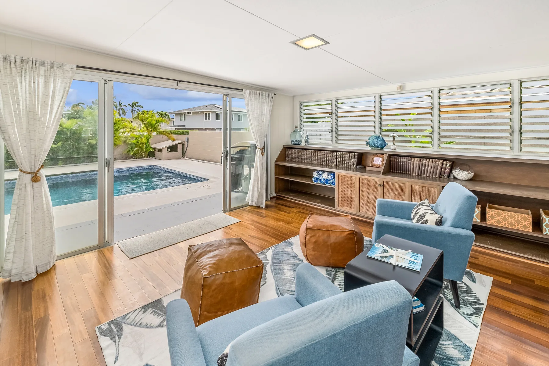 A bright living room with blue seating, a low table, and sliding doors opening onto a pool.