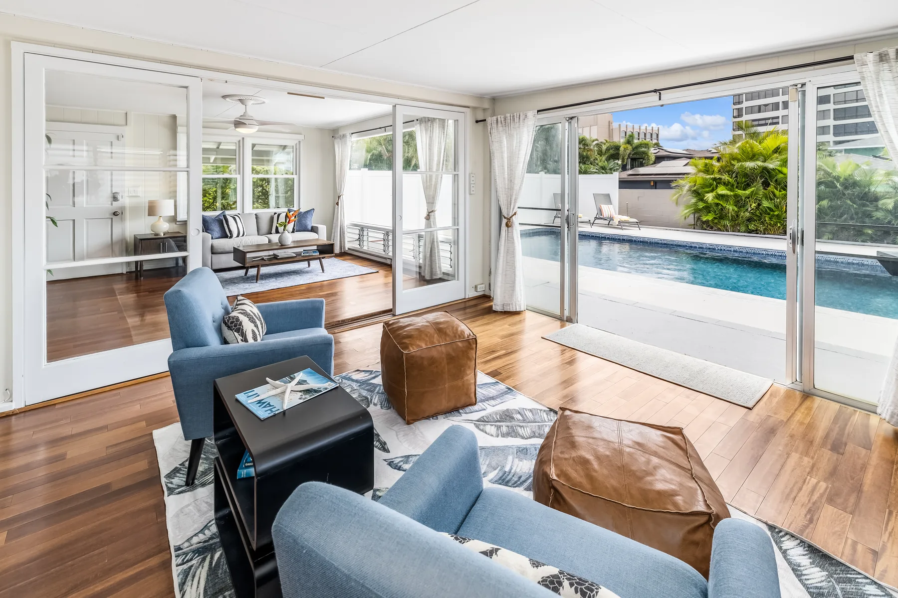 A bright living room opens through glass doors onto a poolside patio.