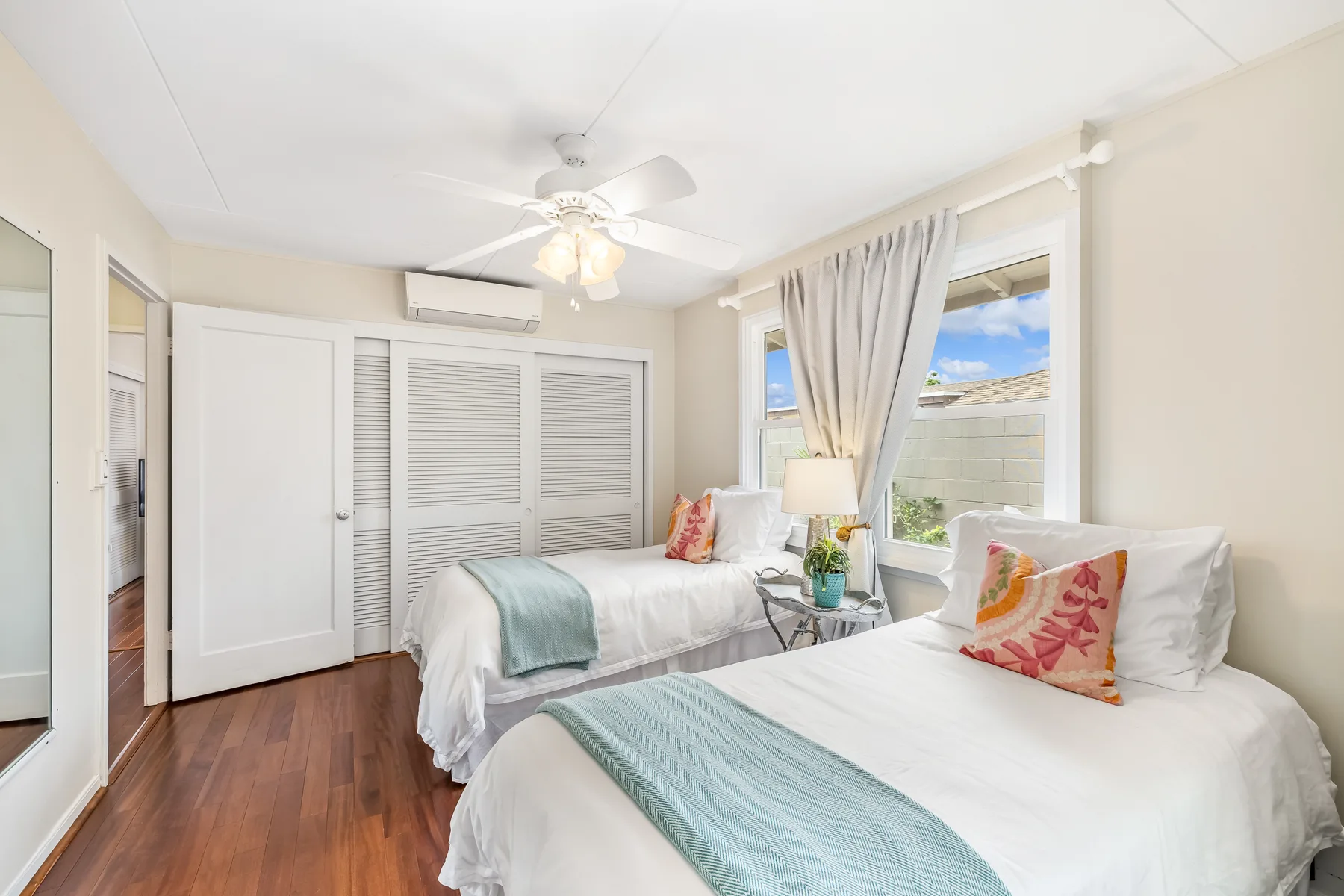 A bright bedroom with two beds and windows overlooking a walled outdoor area.