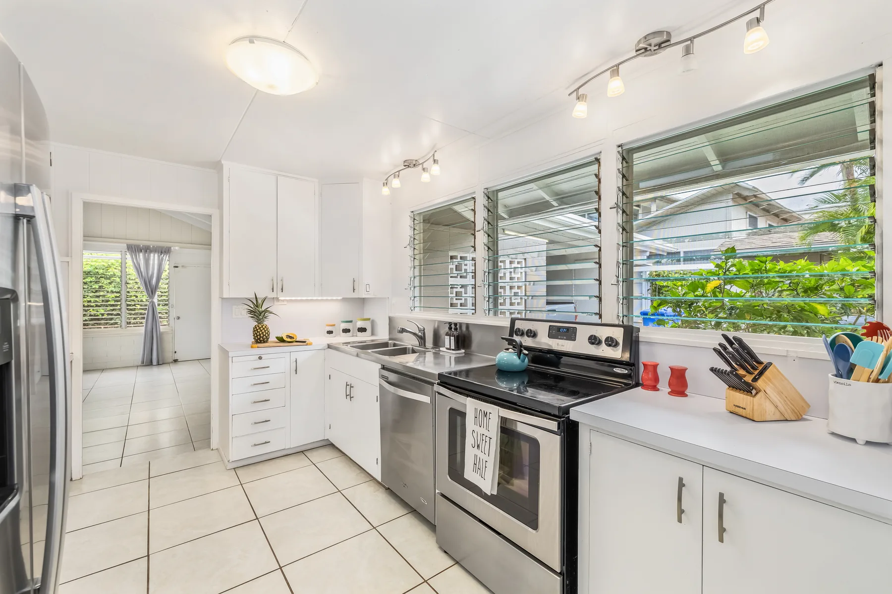 A bright kitchen with white cabinets, stainless steel appliances, and windows overlooking greenery.