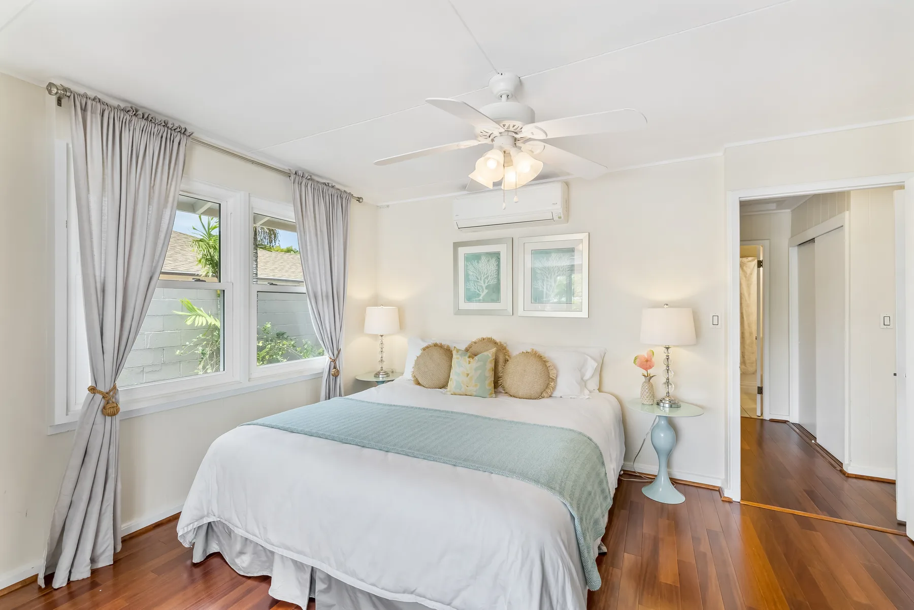 A bedroom with a bed beneath two framed pictures and windows along the wall.