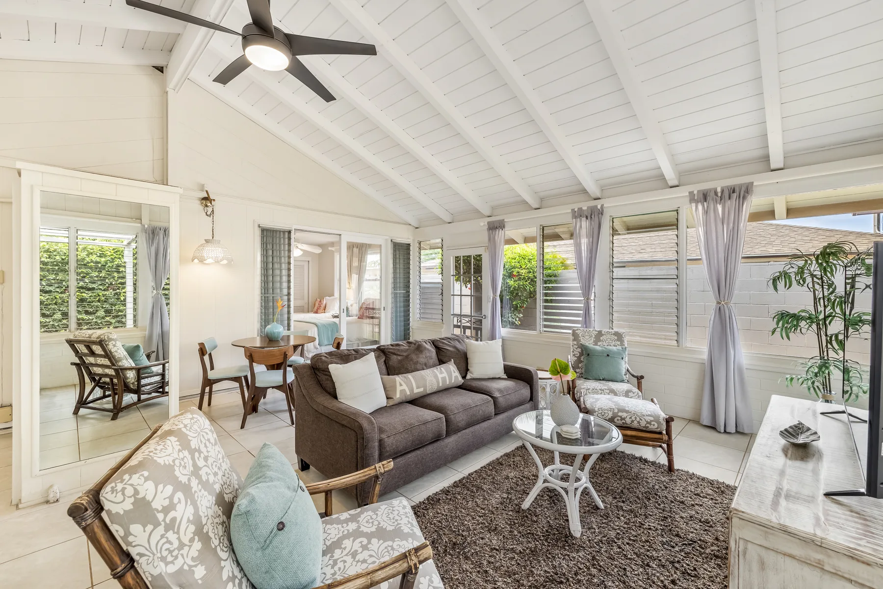 A bright living room with seating around a glass coffee table and windows overlooking greenery.