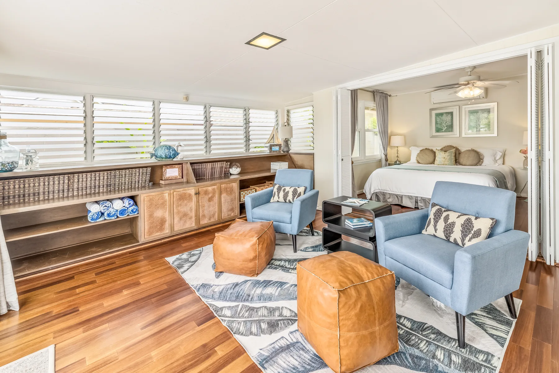 A bright living area has blue seating, a patterned rug, and a long wooden cabinet.