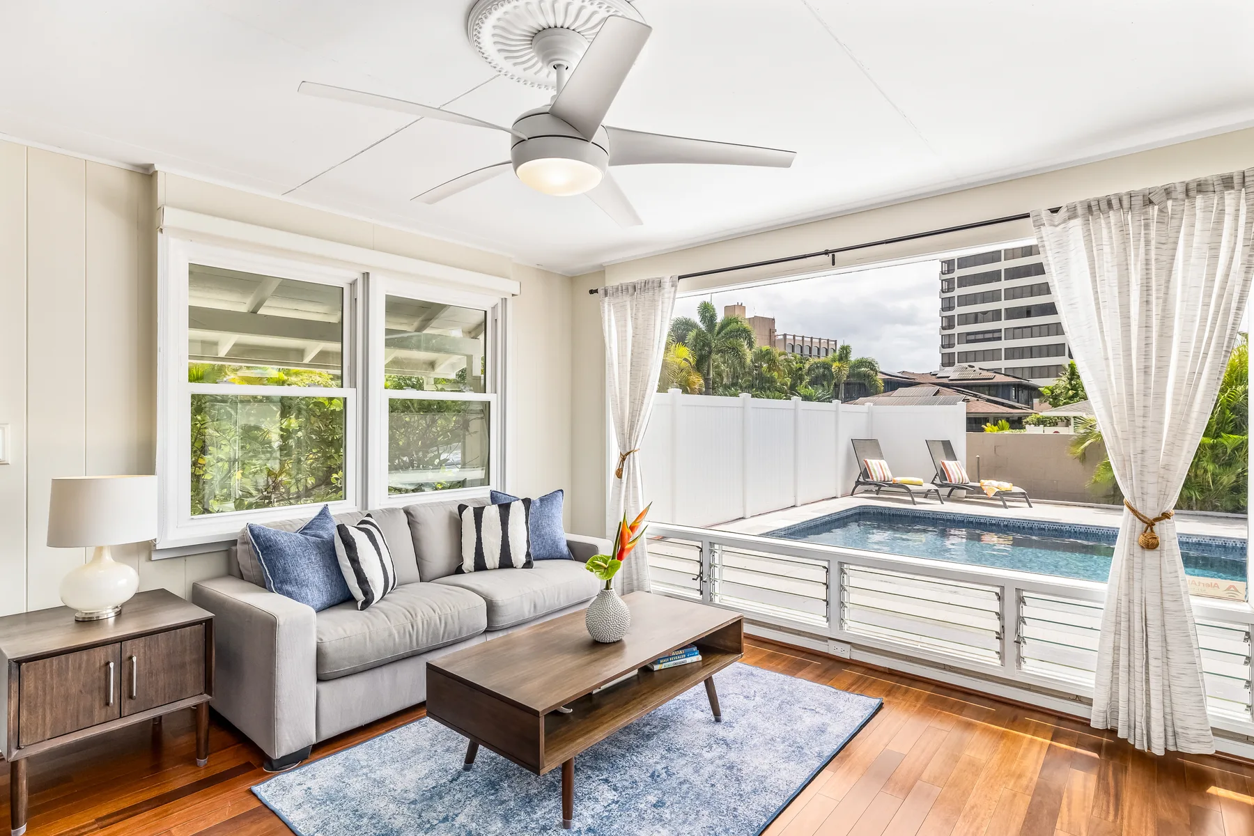 A bright living room opens onto a poolside terrace, with a sofa and coffee table.