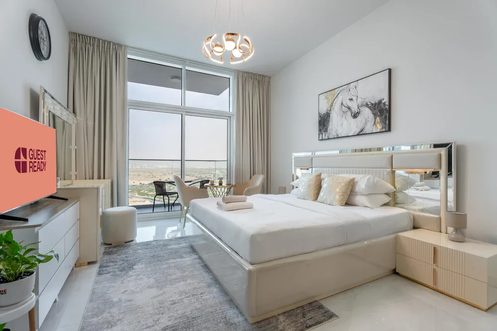 A bright bedroom with a large bed, mirrored headboard, and tall windows.