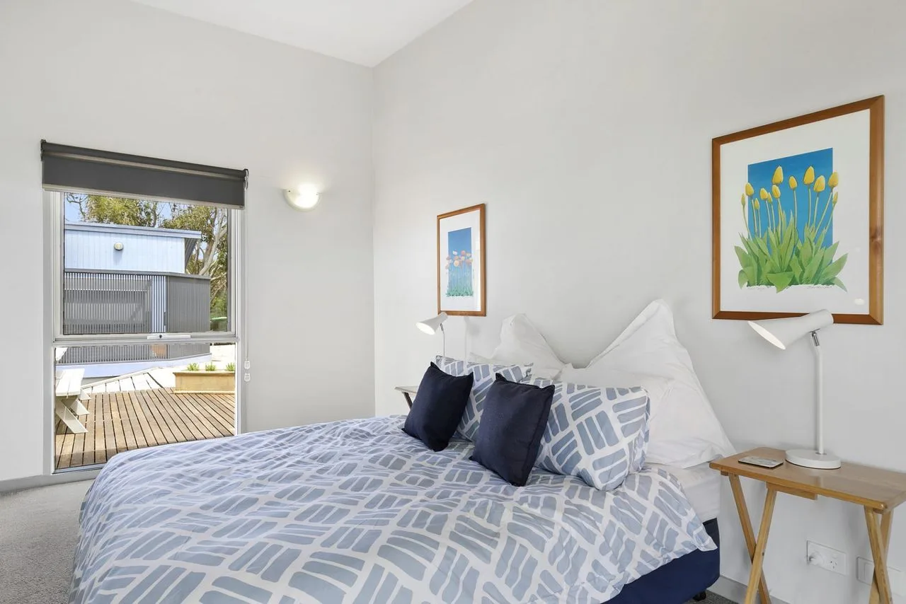 Dormitorio con una cama bien arreglada y una ventana abierta hacia una terraza.