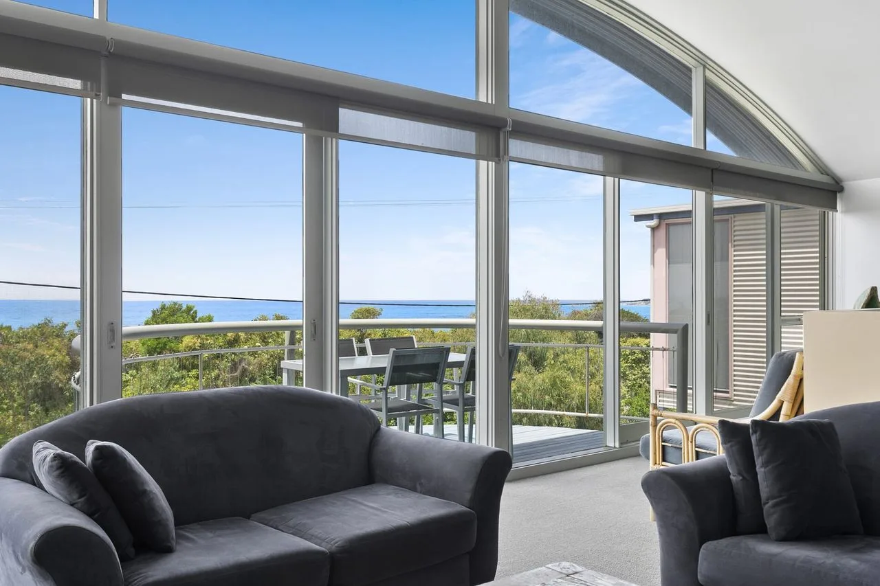 Una sala de estar con asientos junto a grandes ventanas con vistas a la vegetación y al mar.