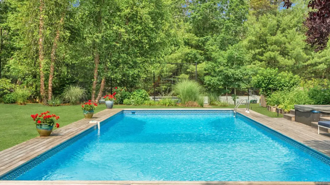 Una piscina al aire libre está rodeada de vegetación y una terraza de madera.