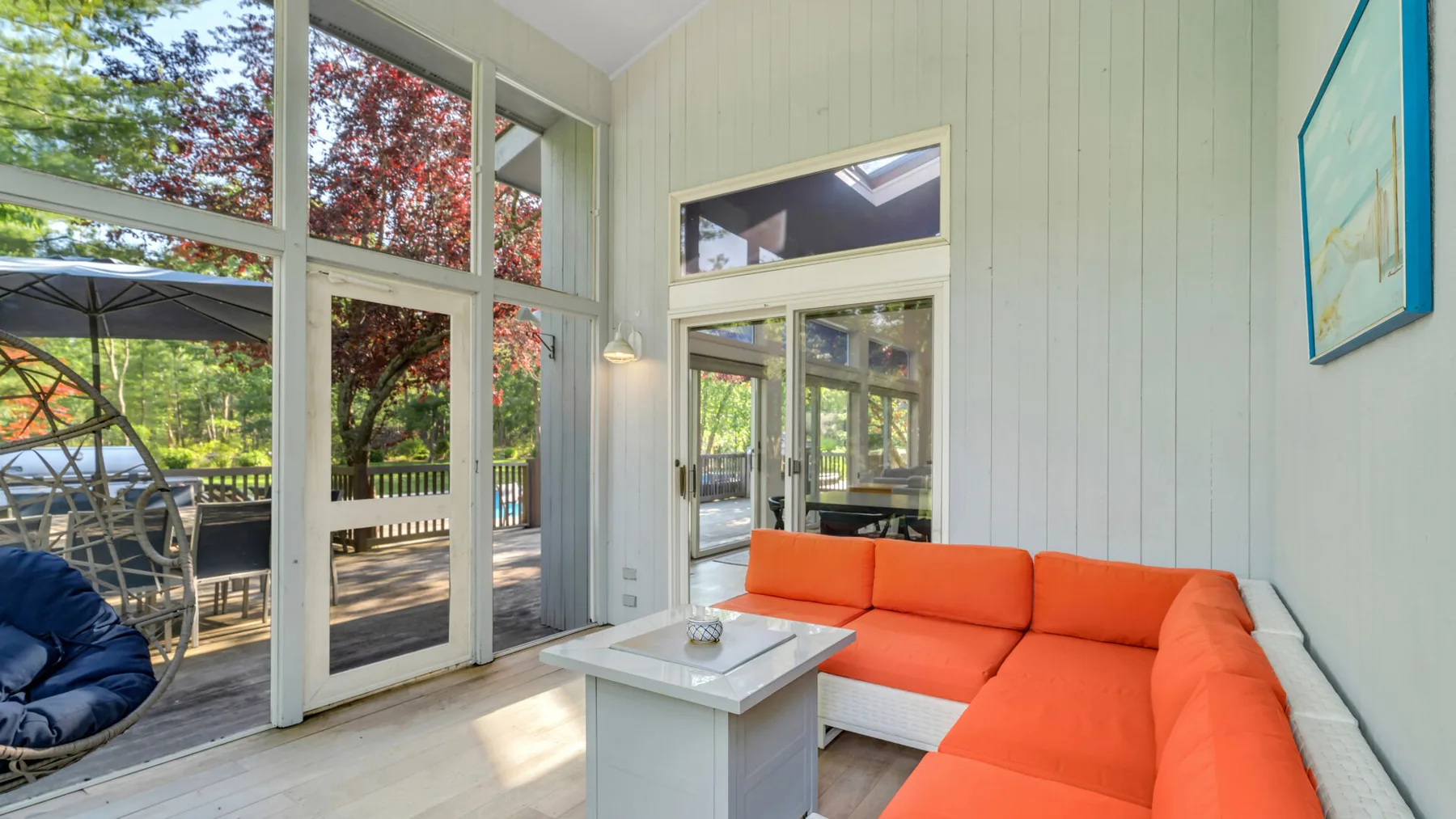 Una sala luminosa con asientos naranjas junto a grandes ventanas que dan a una terraza.