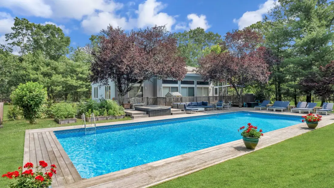 Una piscina al aire libre junto a una casa moderna, con árboles y jardineras con flores.