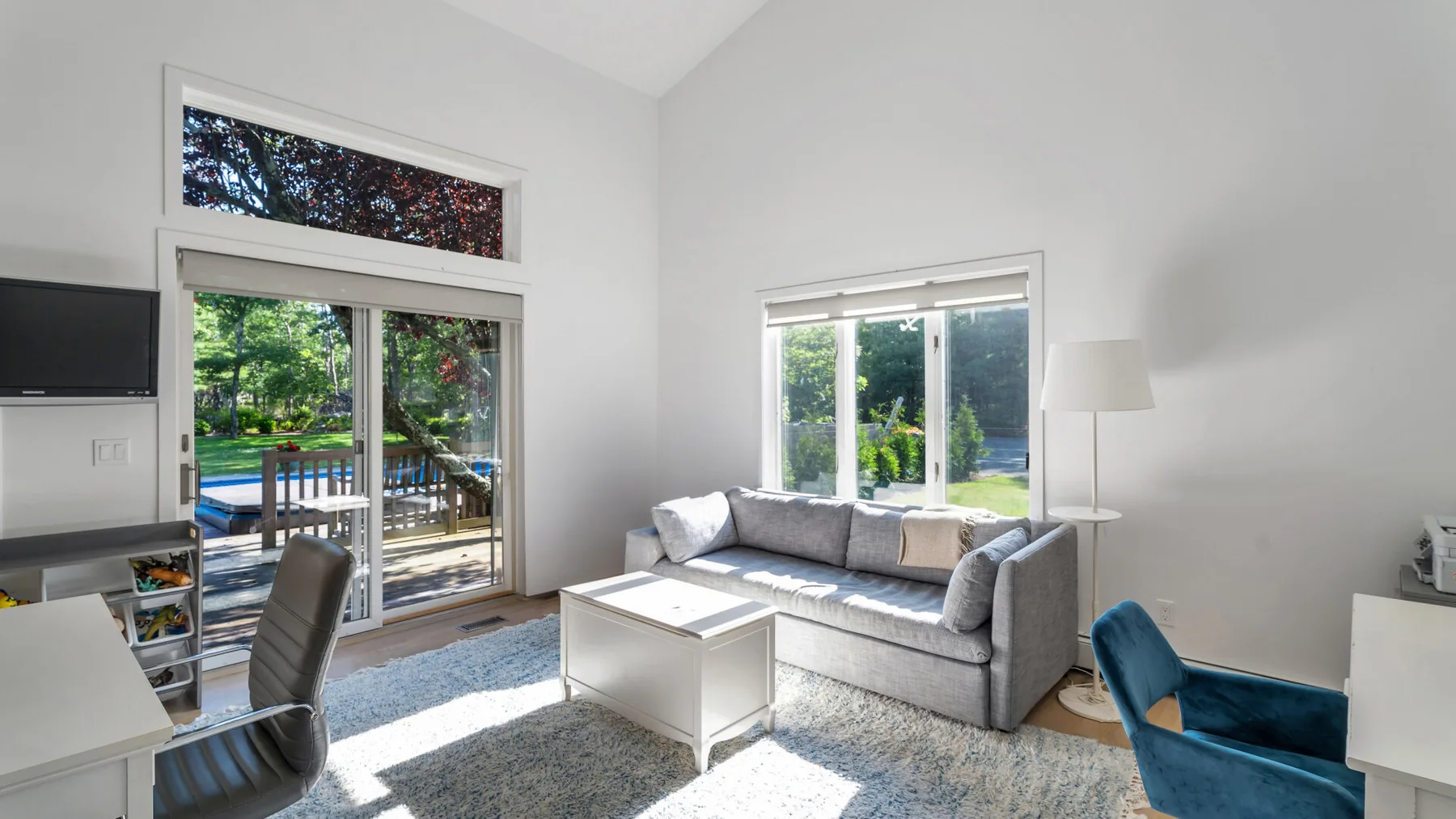 Una sala de estar luminosa con un sofá gris junto a grandes ventanas.