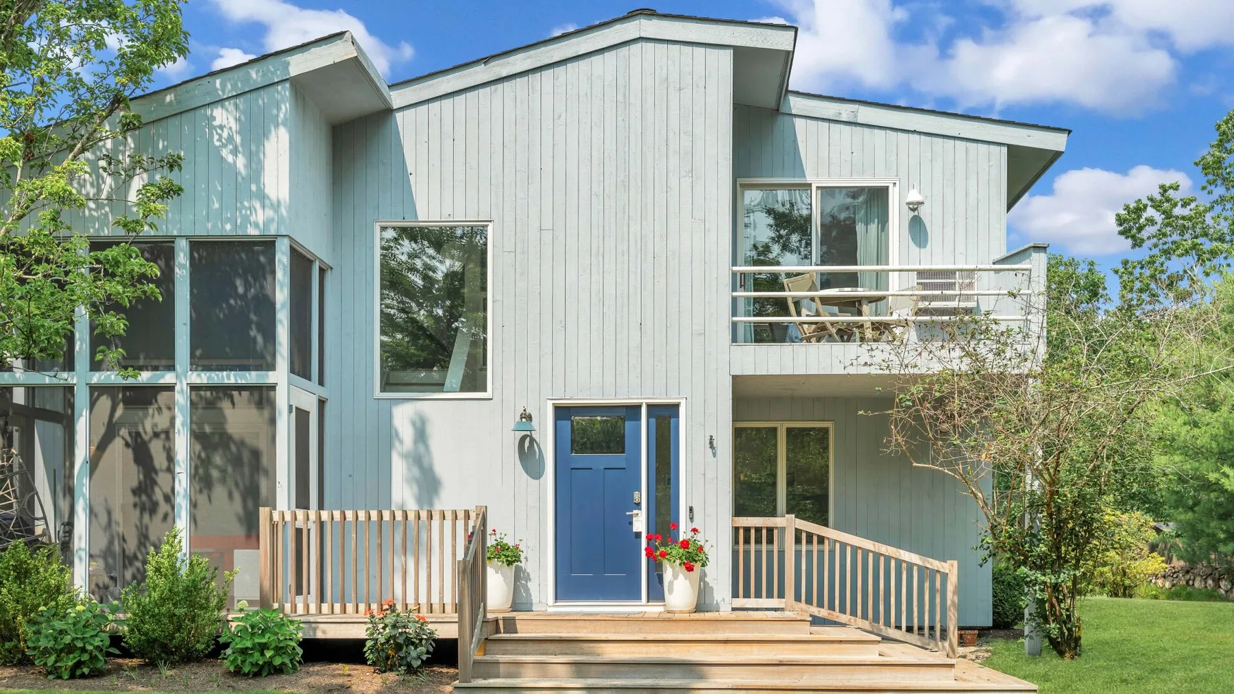 Exterior de una casa moderna con puerta azul y terraza de madera.