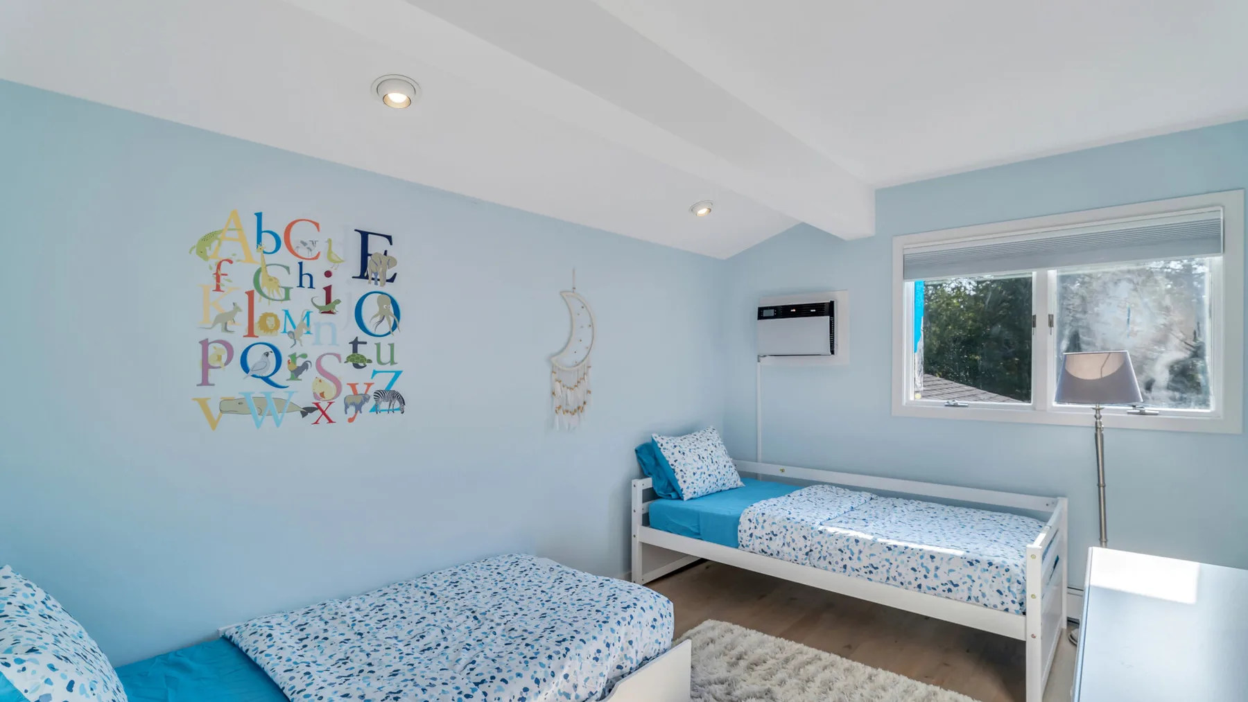 Un dormitorio luminoso tiene dos camas con ropa de cama azul estampada y letras decorativas en la pared.