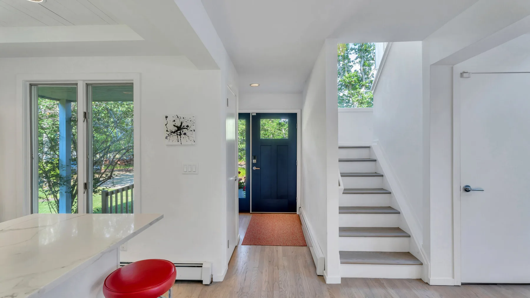 Una entrada luminosa con una puerta azul y una escalera al lado.
