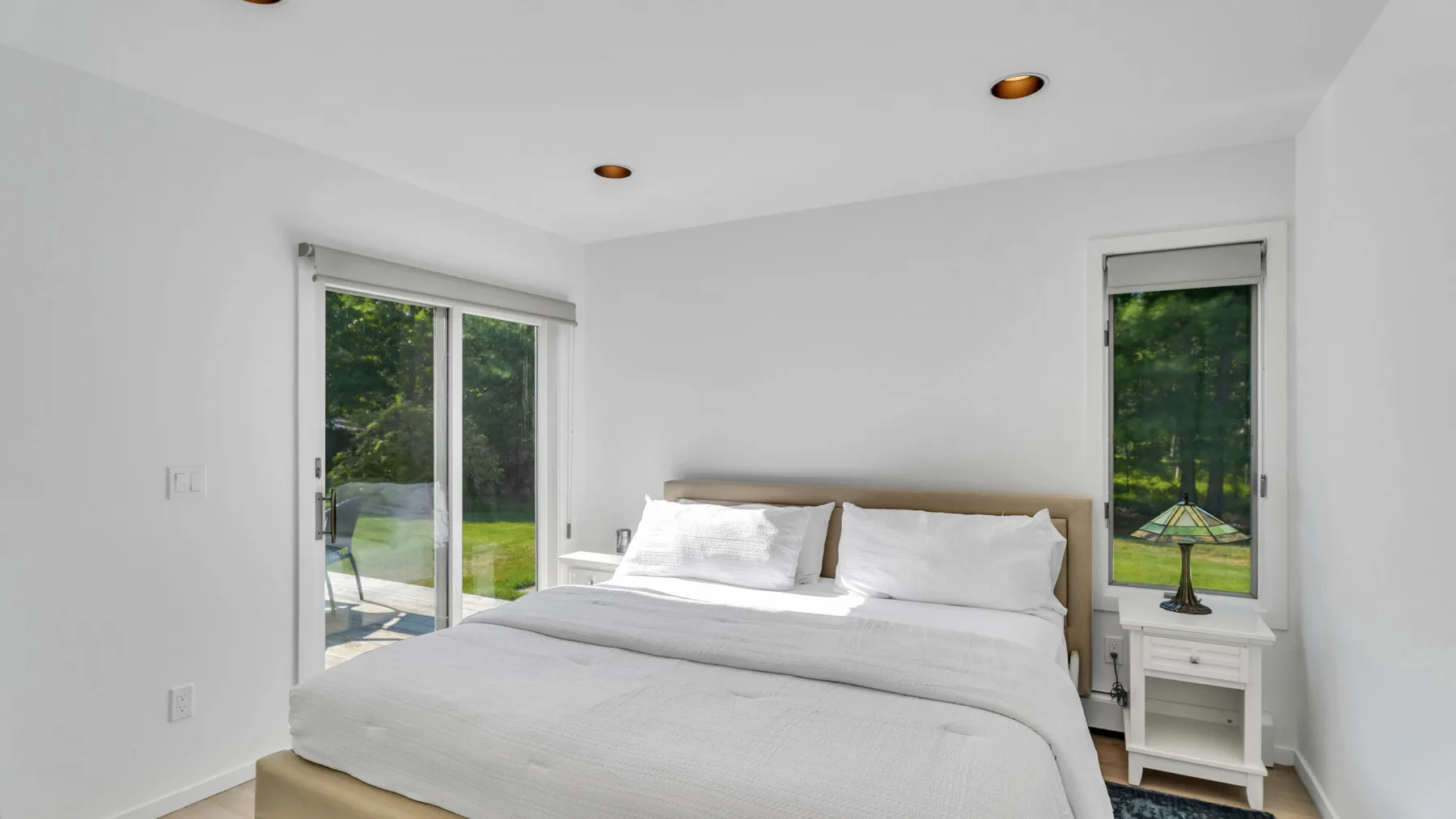 Un dormitorio luminoso con una cama tendida y ventanas con vistas a la vegetación.