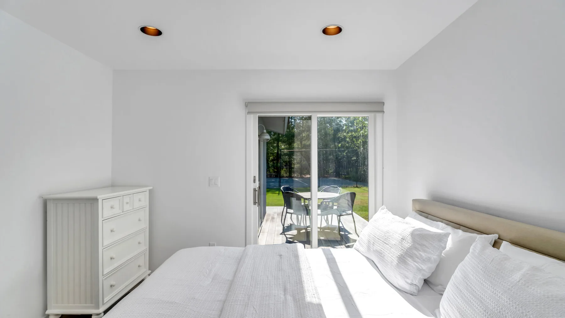 Un dormitorio luminoso con cama, cómoda y puertas de vidrio que dan a un patio.