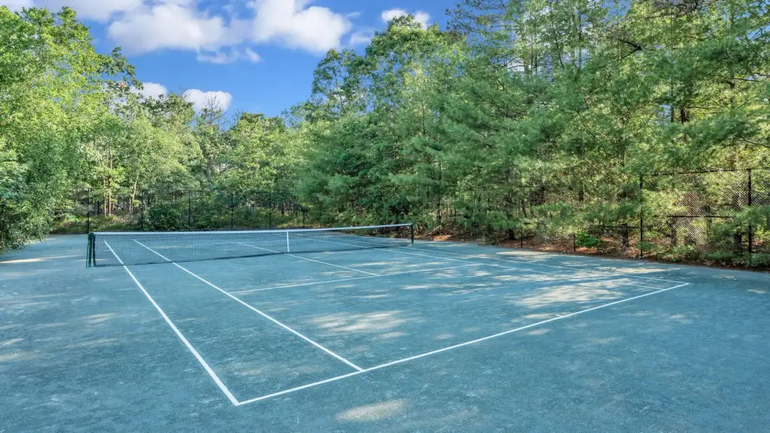 Una cancha de tenis rodeada de árboles bajo un cielo parcialmente nublado.