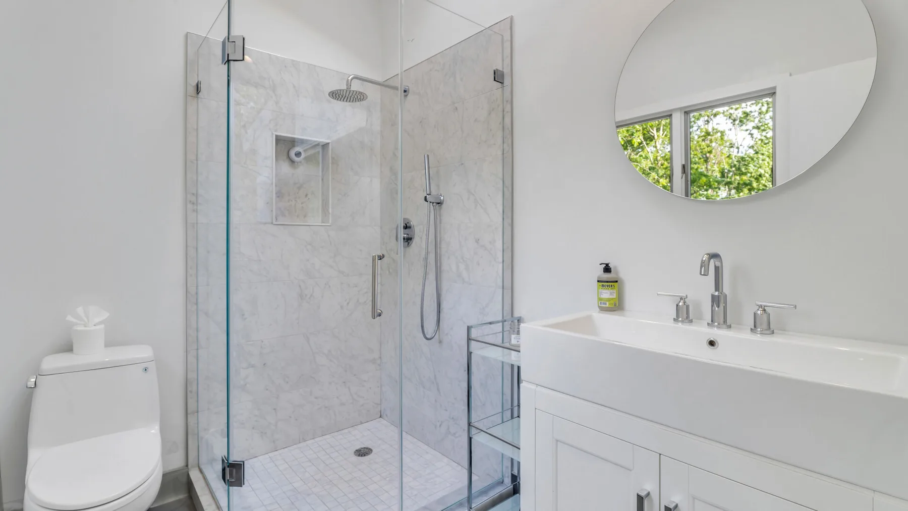 Un baño moderno con ducha de vidrio, tocador y espejo redondo.
