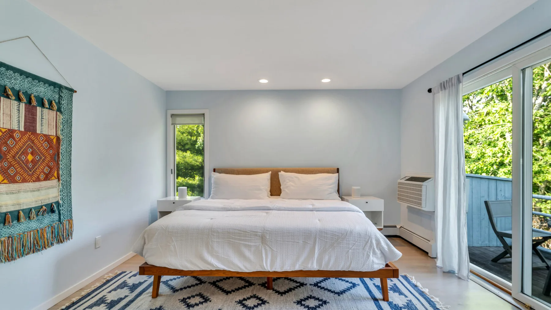 Un dormitorio con una cama tendida, una alfombra estampada y puertas corredizas de vidrio.