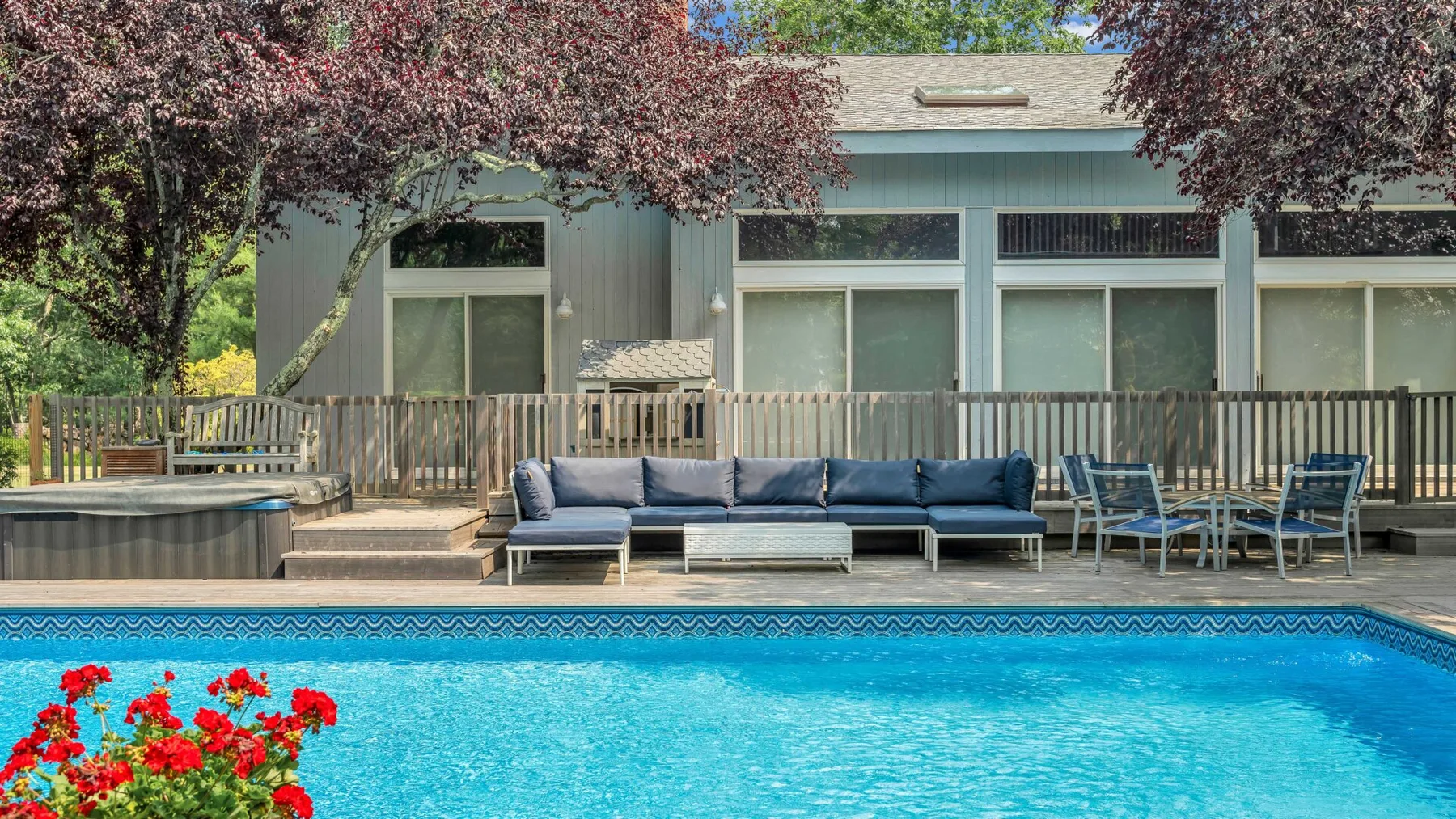 Una piscina exterior está junto a una terraza con asientos y un edificio de color claro.
