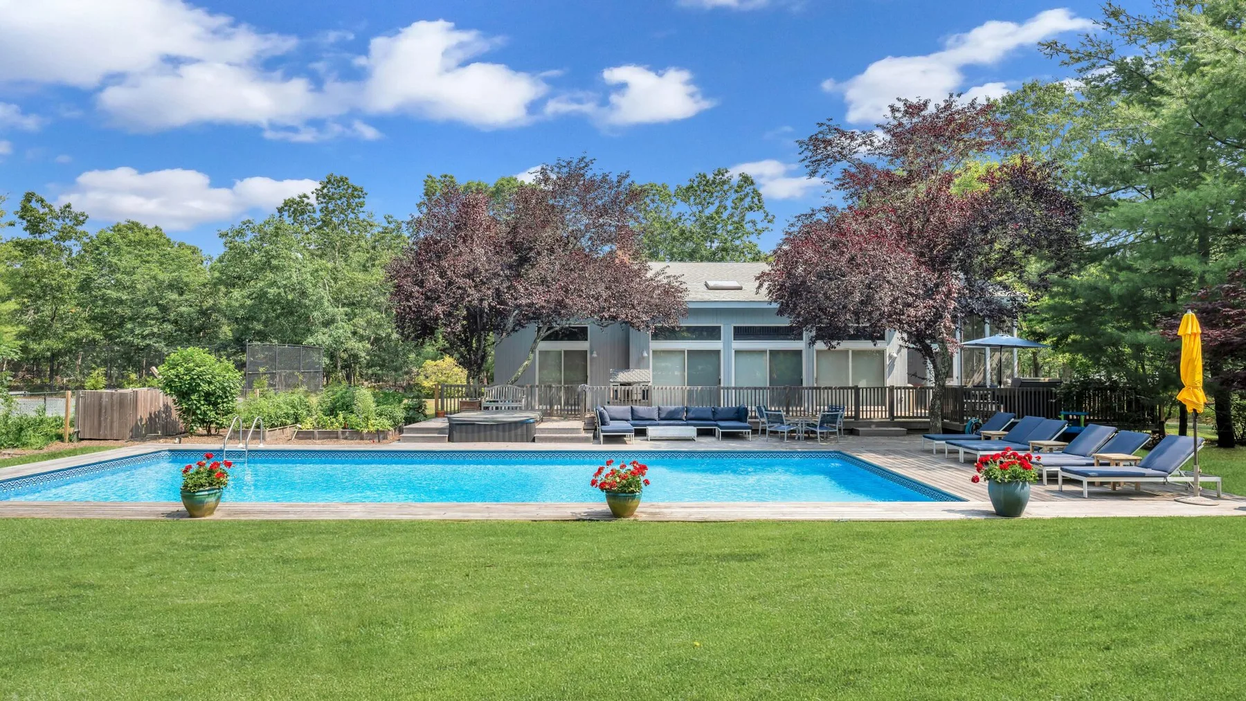 Una piscina al aire libre junto a un césped, con asientos y árboles alrededor del patio.