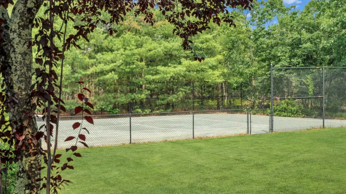 Una cancha de tenis al aire libre, junto a un césped verde y árboles.