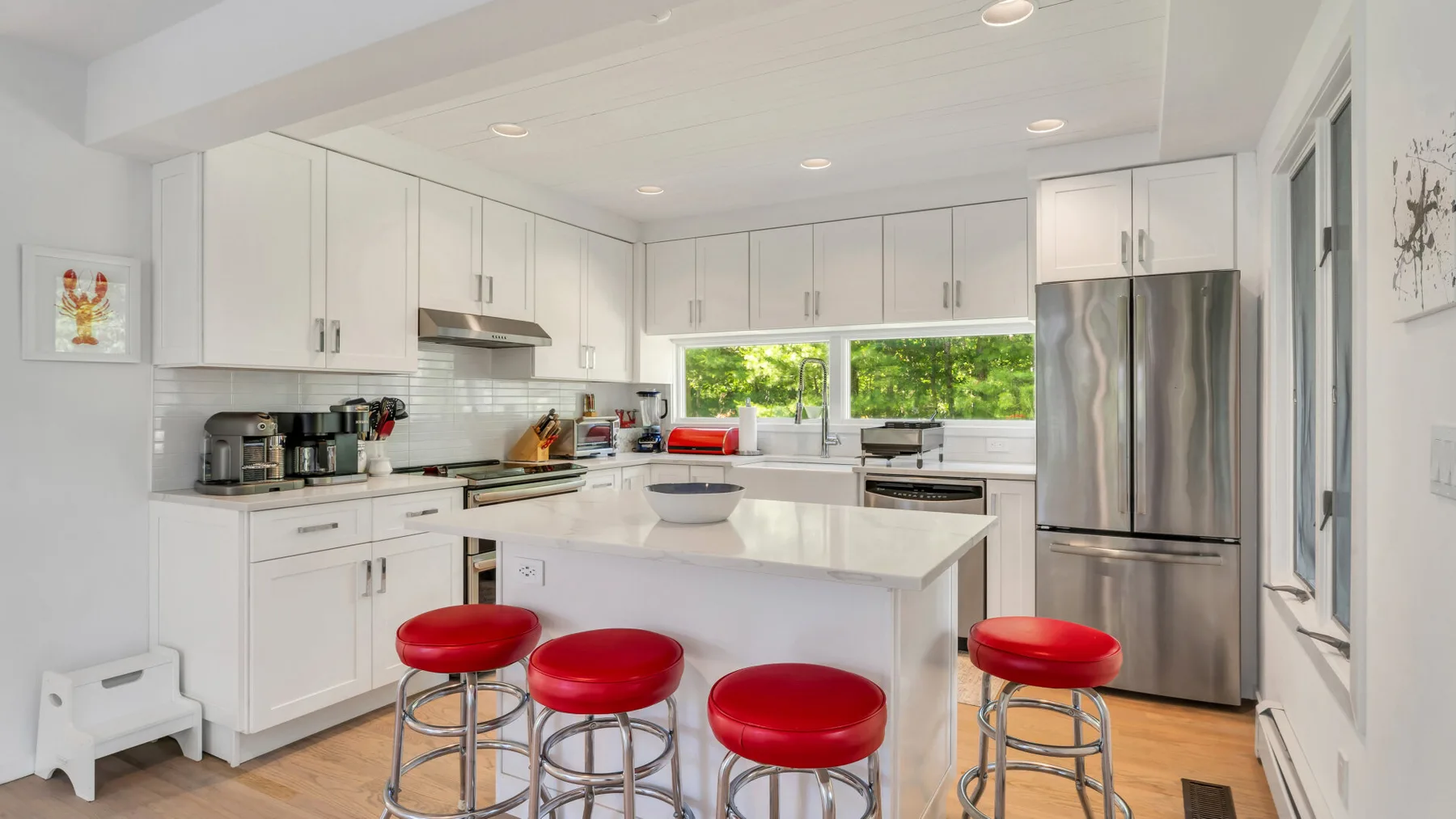 Una cocina blanca y luminosa con una isla central y taburetes rojos.