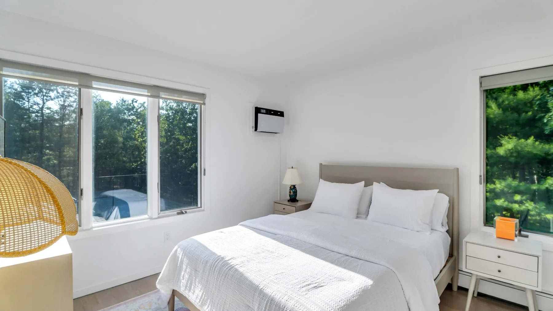 Un dormitorio luminoso con una cama bien arreglada y grandes ventanas con vistas a la vegetación.
