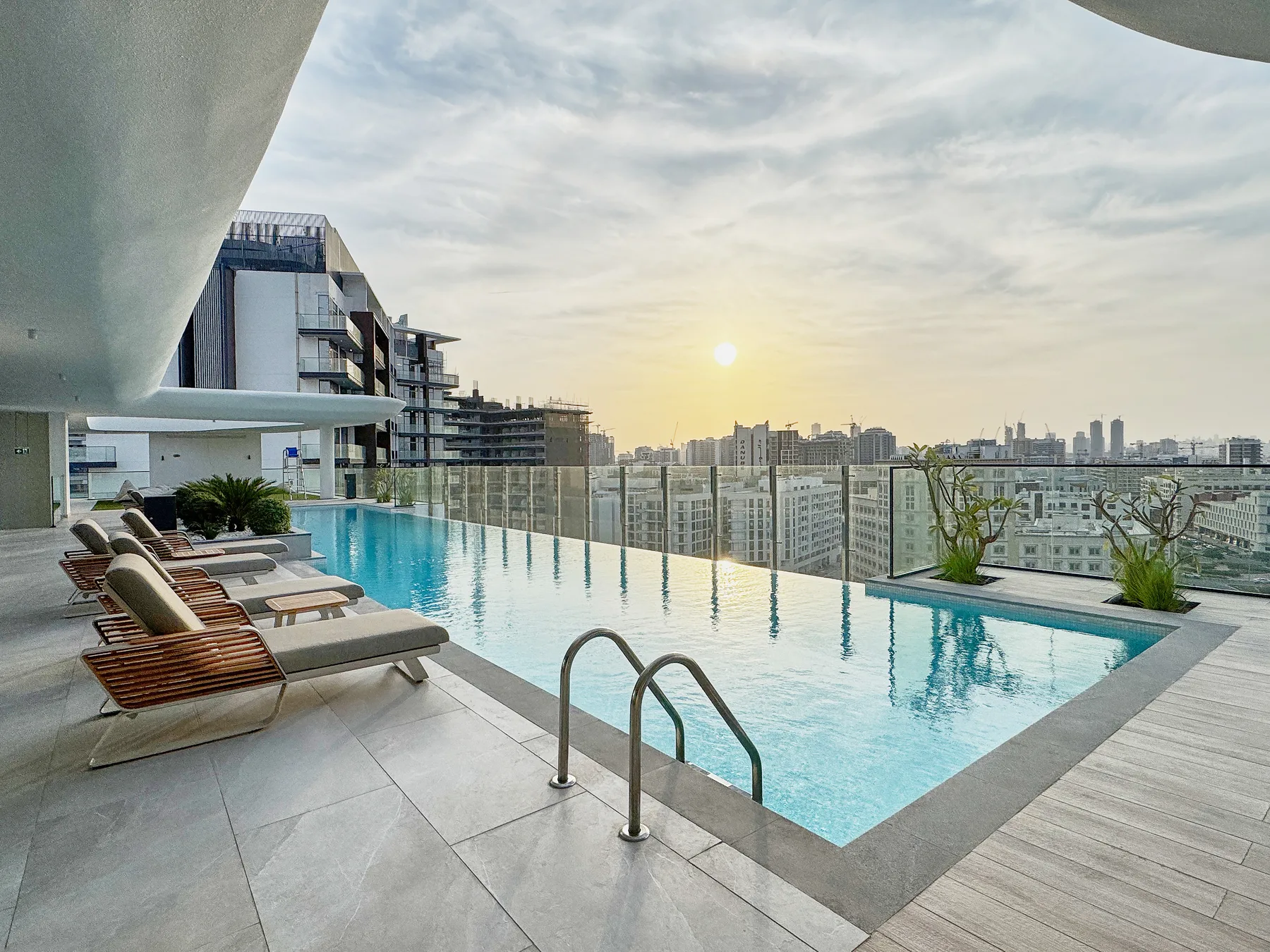 A rooftop swimming pool overlooks the city skyline at sunset.