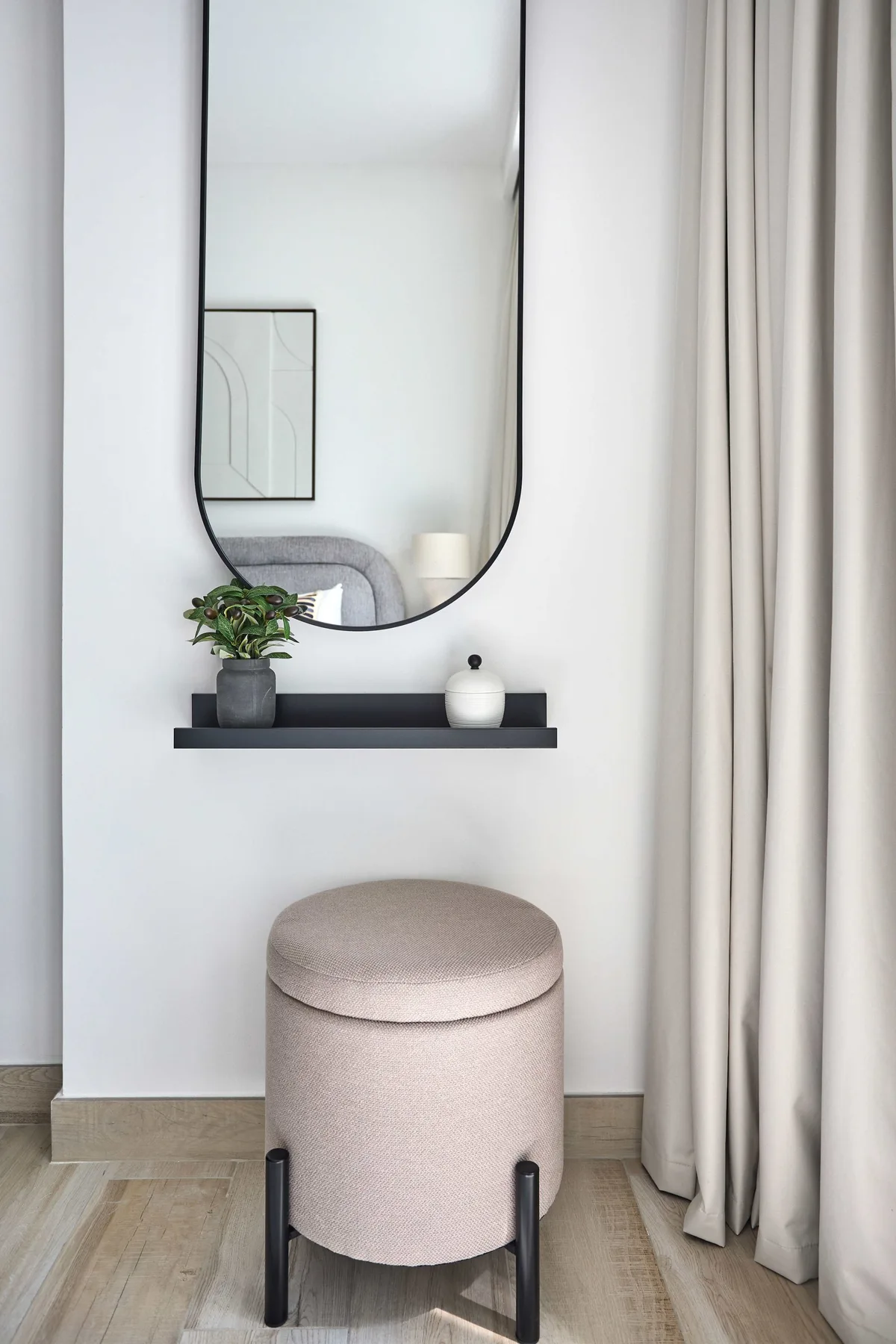 A small upholstered stool sits beneath a wall mirror and narrow shelf.