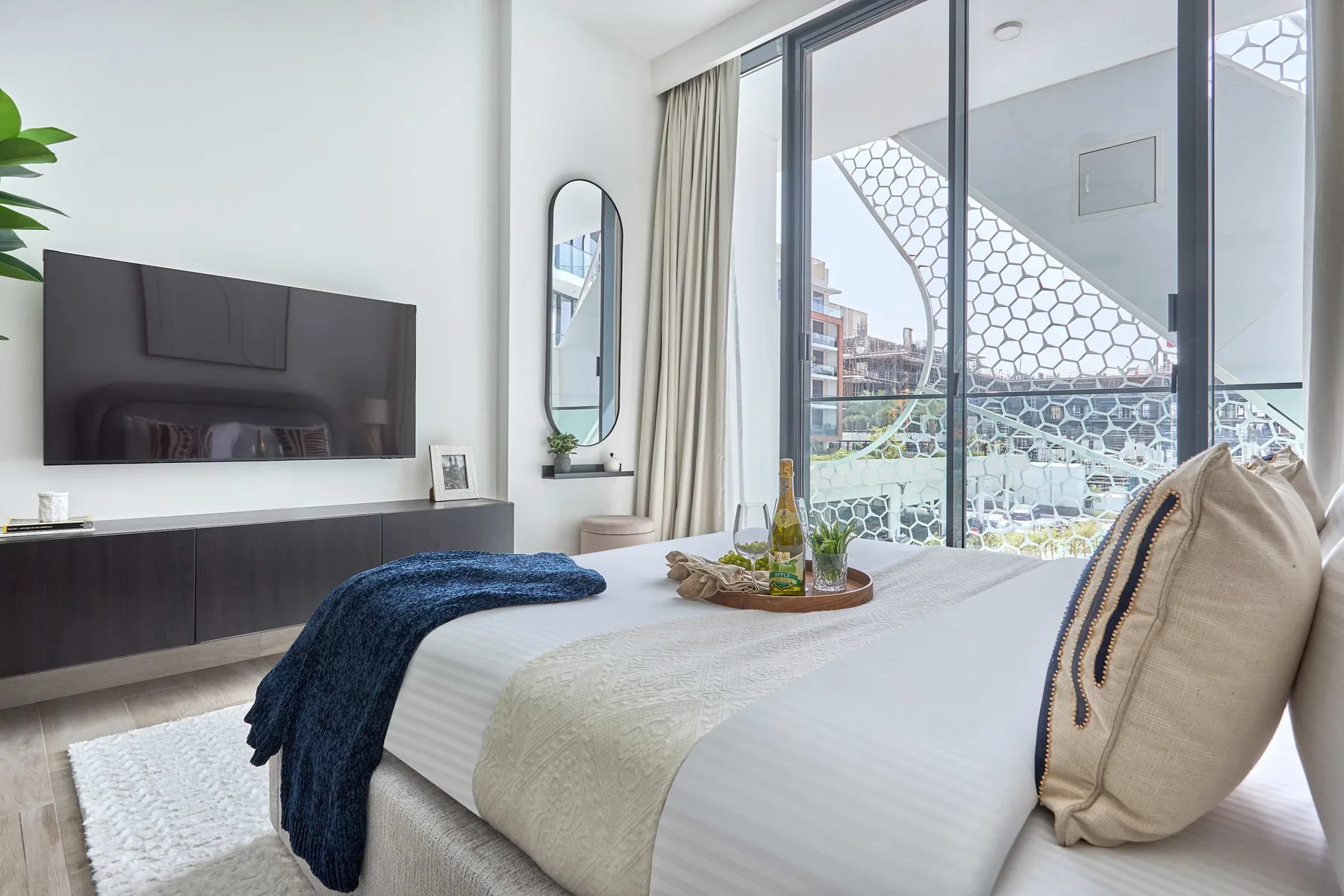 A bright bedroom with a bed beside floor-to-ceiling windows.